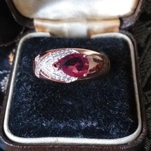 May include: A red gemstone ring set in a gold band with small diamonds surrounding the stone. The ring is in a velvet-lined box with the inscription "Hancock & Jones (Goldsmiths) Ltd. 29 King Street, St. Anne's Passage, Manchester. Phone: Blackfriars 4512."