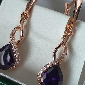 Peut inclure: Une paire de boucles d'oreilles en or rose avec une pierre précieuse violette en forme de larme et un design torsadé accentué de pierres de zircone cubique transparentes.