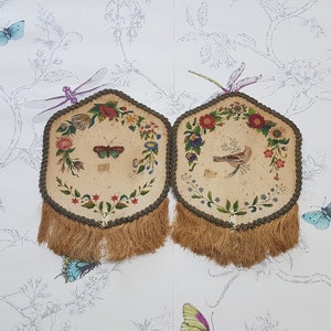 May include: Two hexagonal embroidered wall hangings with a floral and bird design. Each hanging has a brown fringe and features a different bird or butterfly.