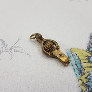 May include: A brass nutcracker with a decorative design. The nutcracker is in the shape of a small, ornate cage with a hinged lid. The nutcracker is closed, and the lid is slightly ajar.