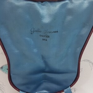 May include: A blue velvet jewellery box with a burgundy trim. The box has the text "Giulio Bocconi" and "OREFICE BRA" printed on the inside.