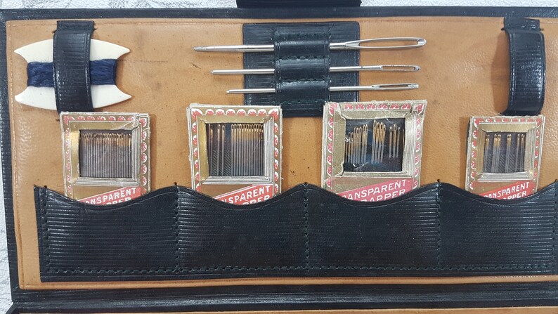 May include: A brown leather sewing kit with four compartments containing needles and thread. The kit has a black strap and a white spool holder.