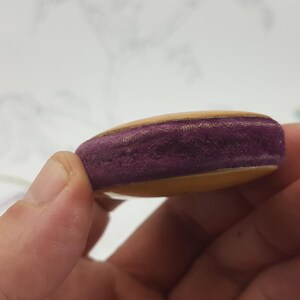 May include: A small, round, wooden object with a purple velvet center. The object is held in a hand.