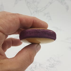 May include: A purple and beige macaron cookie held in a hand.