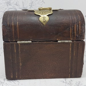 May include: A small, brown leather box with a brass latch and hinges. The box has a decorative design on the top and is closed.