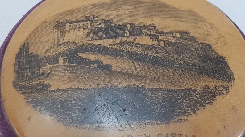 May include: A close-up of a wooden trinket box with a brown background and a black and white image of a castle on a hill. The text "EDINBURGH CASTLE" is printed at the bottom of the image.