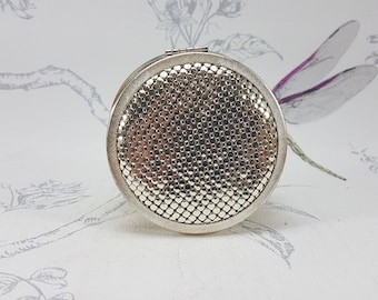 Polvos compactos vintage en tono plateado, tapa de malla y espejo coleccionable.