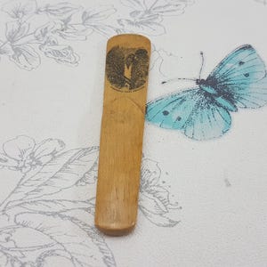 May include: A wooden bookmark with a carved design of a butterfly. The bookmark is light brown and has a smooth finish.