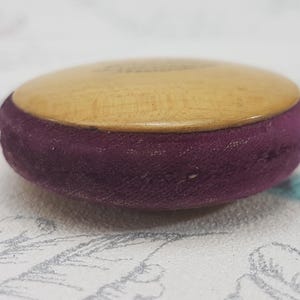May include: A small, round wooden box with a purple velvet lining. The box is about 2 inches in diameter.