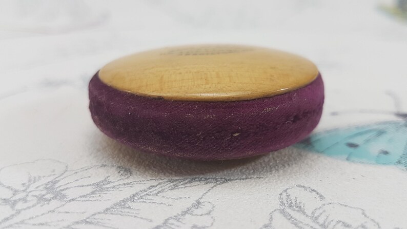 May include: A small, round wooden box with a purple velvet lining. The box is about 2 inches in diameter.