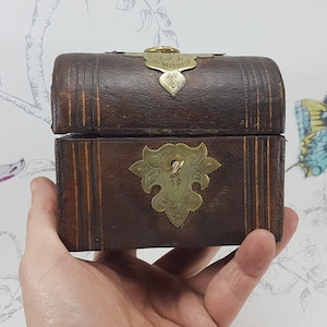 May include: A small, wooden box with a hinged lid and brass accents. The box is decorated with a carved design and has a brass latch.