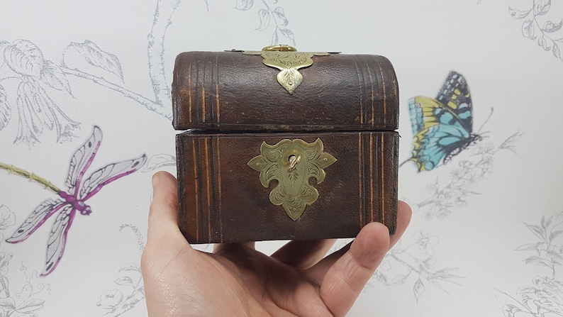 May include: A small, wooden box with a hinged lid and brass accents. The box is decorated with a carved design and has a brass latch.