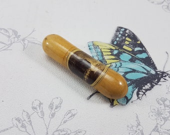 May include: A wooden needle case with a black and white image of a butterfly on the side. The case is a light brown color and has a rounded shape.
