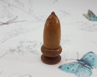 May include: A wooden acorn-shaped bottle stopper with a detailed carved design. The stopper is brown and has a smooth, polished finish.