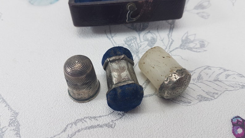 May include: Three silver thimbles, one with a blue velvet top, one with a white top, and one with a silver top.