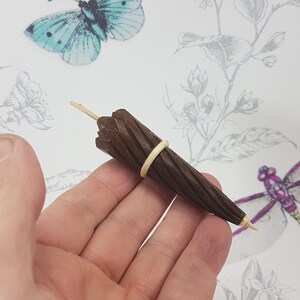 May include: A miniature wooden umbrella with a brown finish and a rubber band around the middle. The umbrella is held in a person's hand.