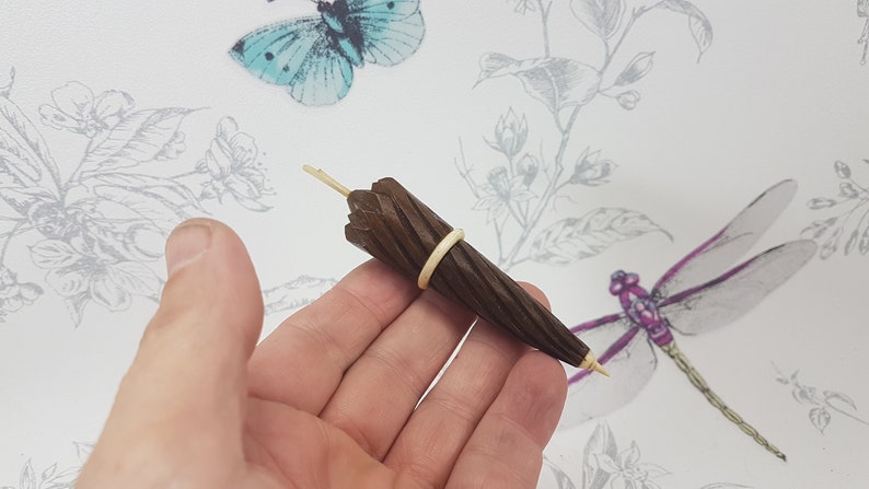 May include: A miniature wooden umbrella with a brown finish and a rubber band around the middle. The umbrella is held in a person's hand.