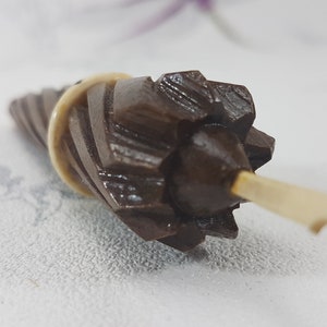 May include: A brown wooden spindle with a decorative, starburst-shaped top and a white plastic handle.