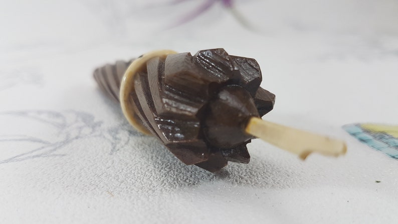 May include: A brown wooden spindle with a decorative, starburst-shaped top and a white plastic handle.