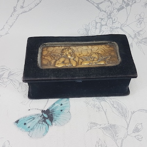May include: A small black velvet box with a gold metal cherub design on the lid.
