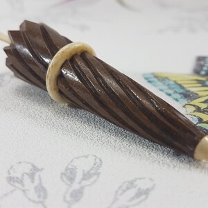 May include: A brown wooden tapered object with a white ring around the middle. The object has a spiral pattern and a pointed tip.