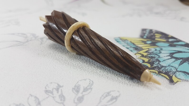 May include: A brown wooden tapered object with a white ring around the middle. The object has a spiral pattern and a pointed tip.