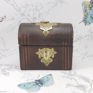 May include: A small, wooden box with a hinged lid and brass accents. The box is decorated with intricate floral designs and has a brass latch.