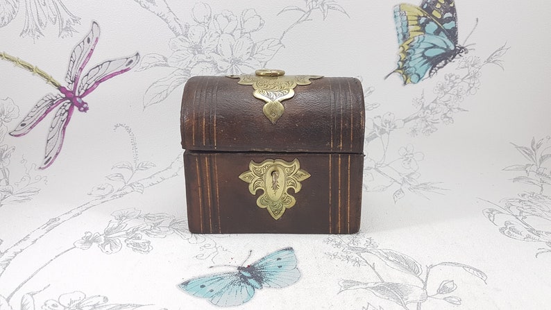 May include: A small, wooden box with a hinged lid and brass accents. The box is decorated with intricate floral designs and has a brass latch.