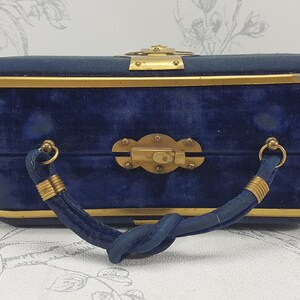 May include: A blue velvet handbag with a gold metal frame and a twisted handle. The bag has a brass clasp and decorative accents.