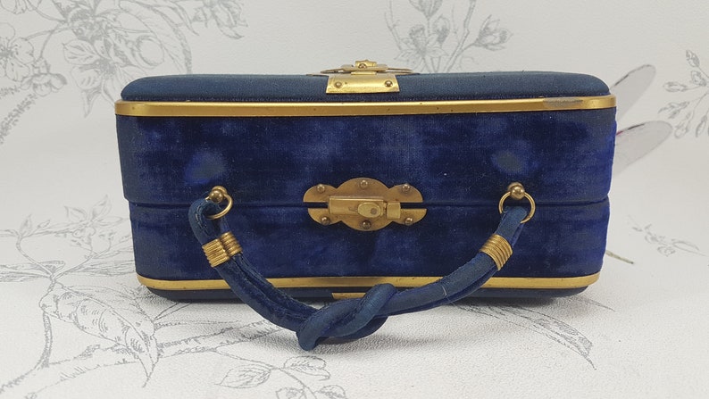 May include: A blue velvet handbag with a gold metal frame and a twisted handle. The bag has a brass clasp and decorative accents.