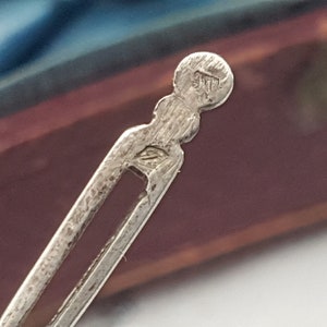 May include: Close-up of a silver metal hair clip with a circular marking that reads "925".