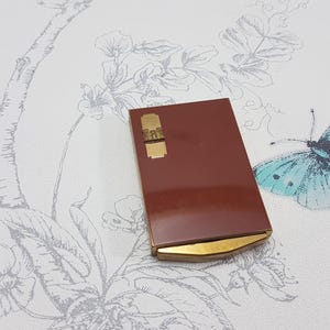 May include: A vintage compact with a gold trim and a brown lid. The compact is closed and has a floral design on the background.