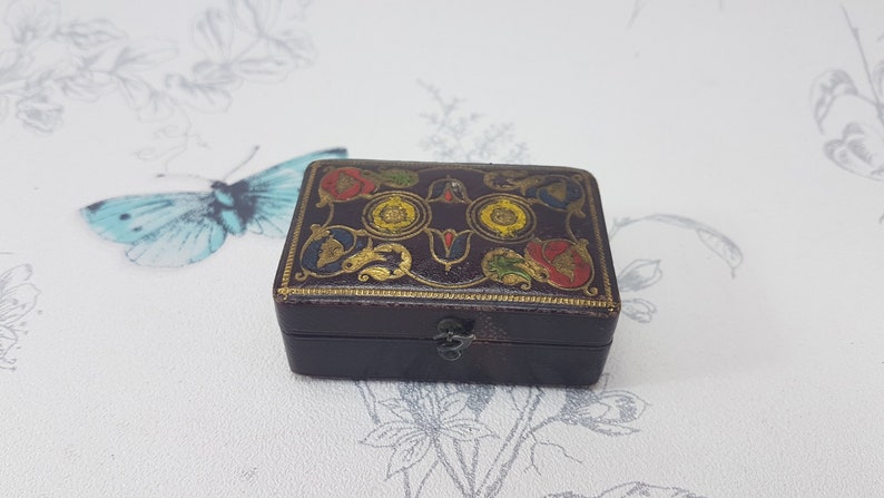 May include: A small, dark brown, rectangular box with a hinged lid. The box is decorated with a colorful floral design in gold, red, yellow, and blue.
