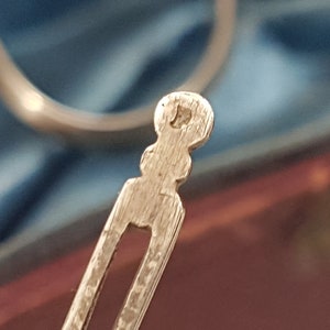 May include: Close-up of the back of a silver hair clip. The clip has a decorative, textured design and a rounded end.
