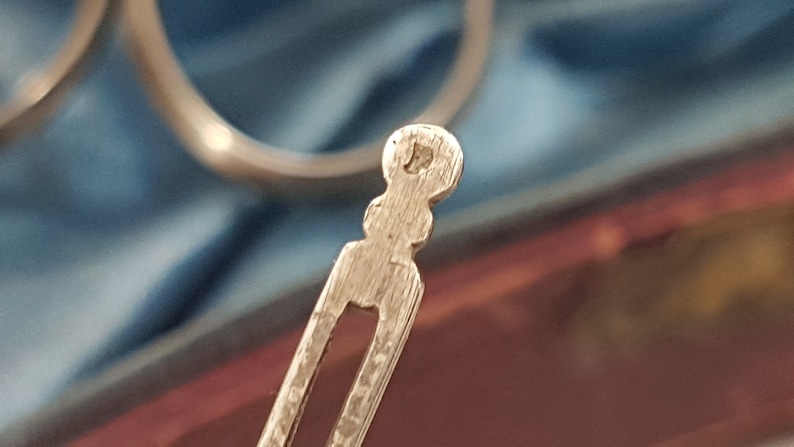 May include: Close-up of the back of a silver hair clip. The clip has a decorative, textured design and a rounded end.
