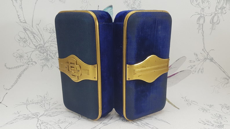May include: A blue velvet jewelry box with gold accents and a hinged closure. The box is open and the interior is lined with blue velvet.