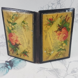 May include: A small, black, hinged box with a floral design. The box is open and the inside is lined with yellow paper featuring a floral design and a poem printed on it. The poem reads, "We gather flowers, sweet, where'er they grow, With gentle hands, and tend them with care, Till the pale buds, on stems so slender, grow, To bloom in beauty, and to scent the air."