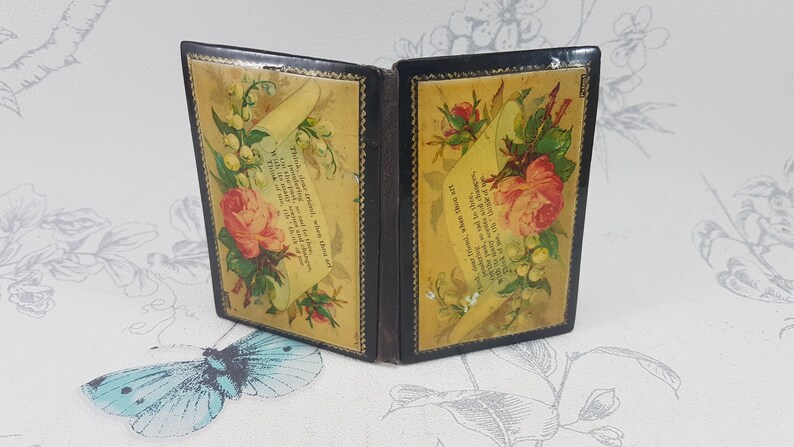 May include: A small, black, hinged box with a floral design. The box is open and the inside is lined with yellow paper featuring a floral design and a poem printed on it. The poem reads, "We gather flowers, sweet, where'er they grow, With gentle hands, and tend them with care, Till the pale buds, on stems so slender, grow, To bloom in beauty, and to scent the air."