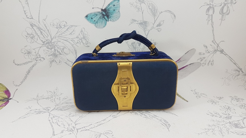 May include: A small, navy blue velvet handbag with a gold clasp and a knotted gold handle.