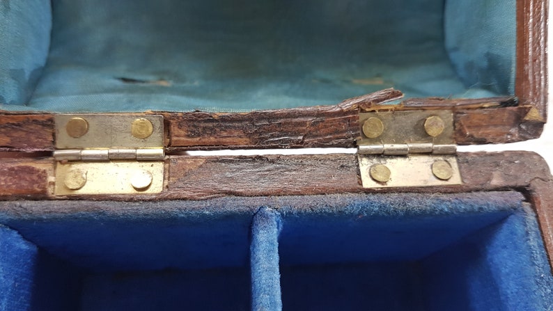 May include: A wooden box with a blue velvet interior and two compartments. The box has brass hinges and is slightly damaged.
