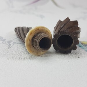 May include: Two vintage wooden thimbles with a spiral design. One thimble has a white plastic top with a threaded hole.