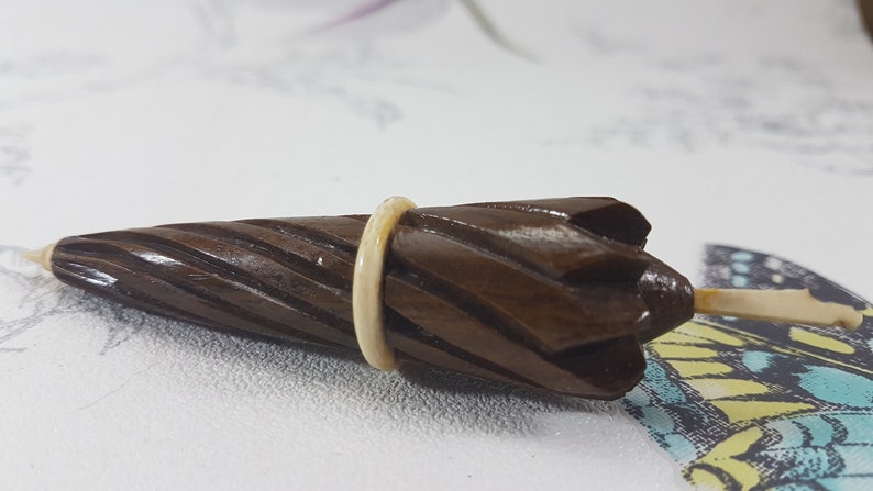 May include: A small, wooden, brown umbrella-shaped object with a white ring around the middle. The object is carved with a spiral pattern and has a pointed tip.