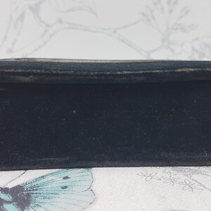 May include: A black velvet box with a smooth, flat surface. The box is closed and has a subtle sheen.