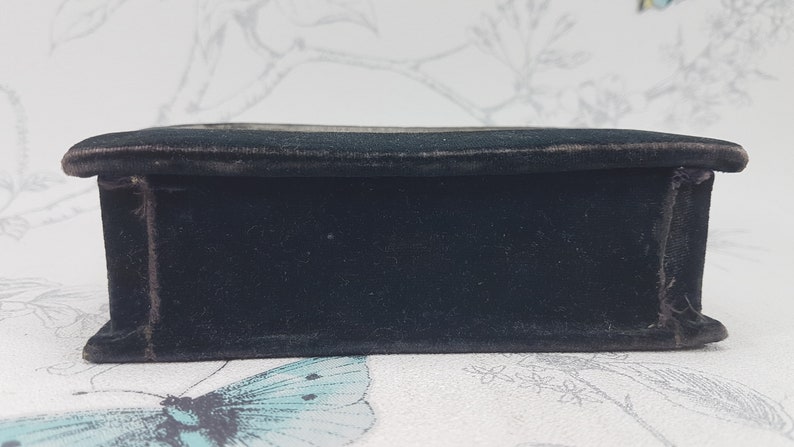 May include: A black velvet box with a smooth, flat surface. The box is closed and has a subtle sheen.