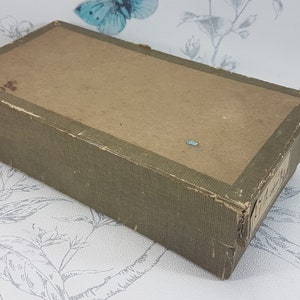 May include: A rectangular box with a green paper covering and a brown paper top. The box is slightly worn and has a few small tears.