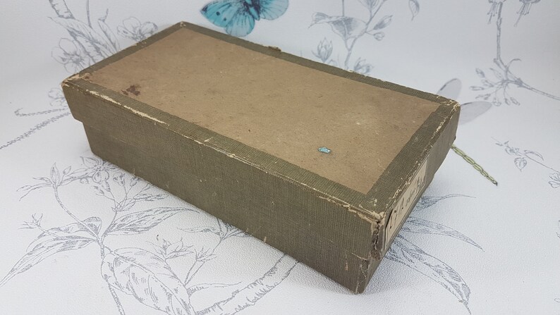 May include: A rectangular box with a green paper covering and a brown paper top. The box is slightly worn and has a few small tears.