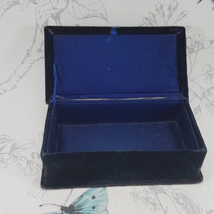 May include: An empty black velvet jewelry box with a blue velvet interior. The box is open and the lid is propped up.