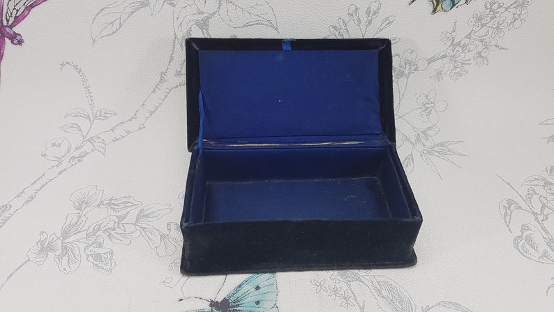 May include: An empty black velvet jewelry box with a blue velvet interior. The box is open and the lid is propped up.