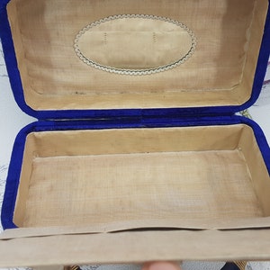 May include: An empty blue velvet jewelry box with a beige interior. The box has a decorative oval design on the lid.