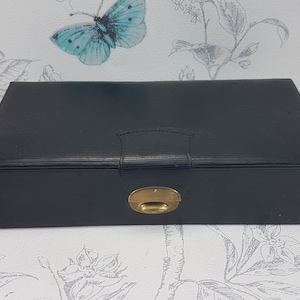 May include: A black leather jewelry box with a gold latch. The box has a textured surface and a raised design on the lid.